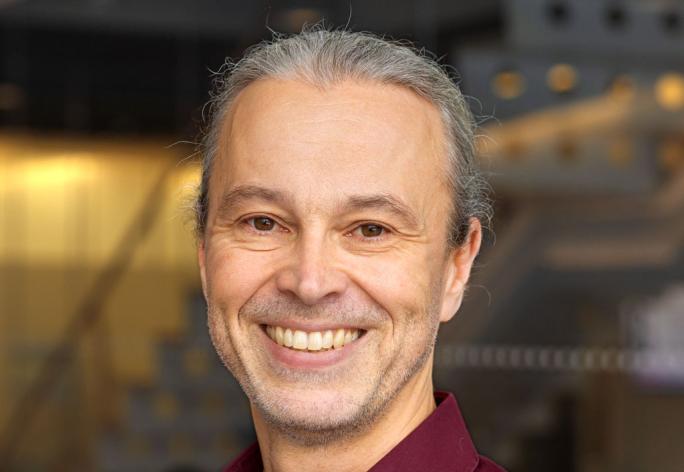 A portrait of Thorsten Joachims, a man with gray hair and a dark red shirt smiling at the camera