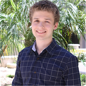 A color photo of a man standing outside, smiling.