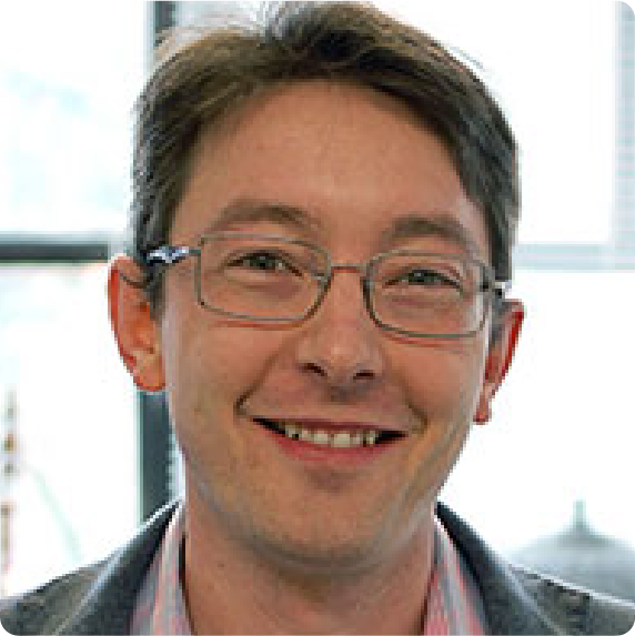 A color photo of a man with glasses smiling for a photo.