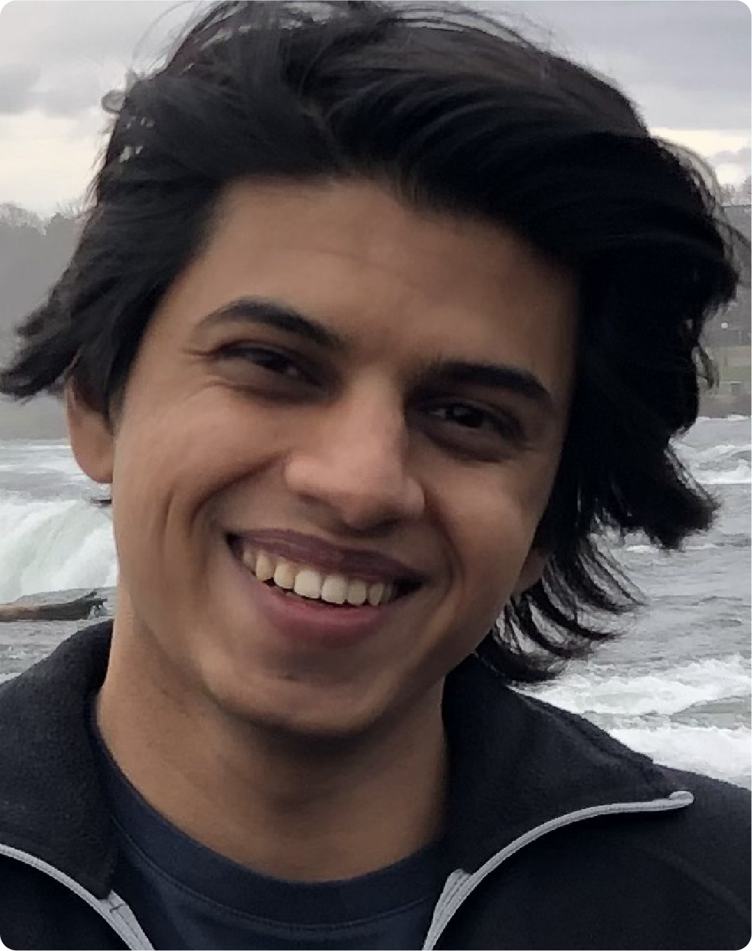 A color photo of a man smiling for a photo near the ocean.