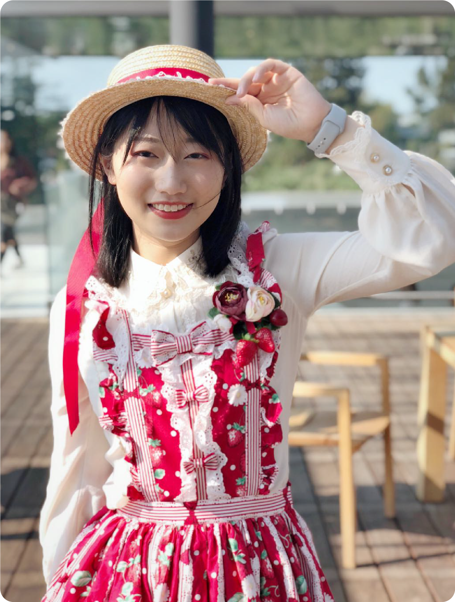 A color photo of a woman wearing a red and white dress while touching her hat, smiling for a photo.