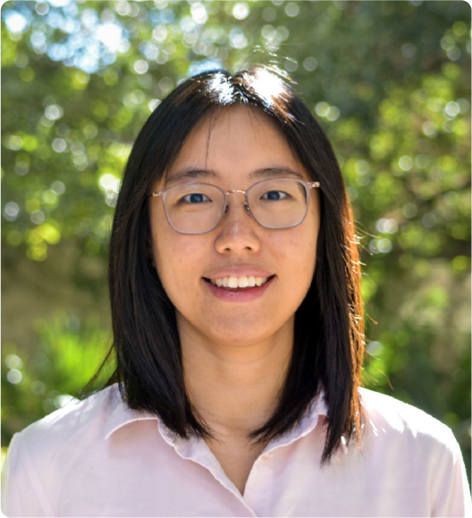 A color photo of a woman with glasses smiling for a photo while outside.