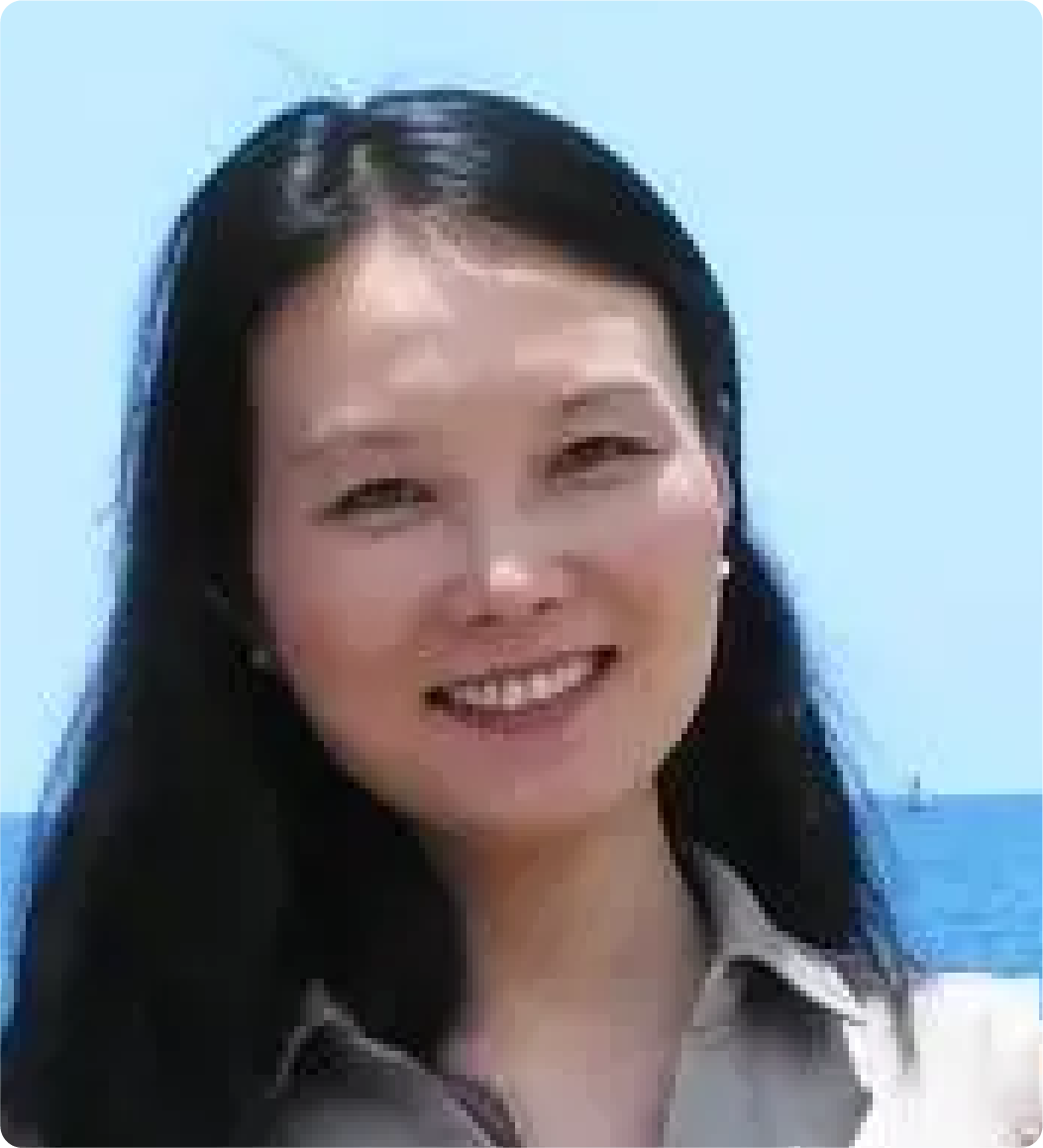 A color photo of a woman smiling for a photo by a body of water.