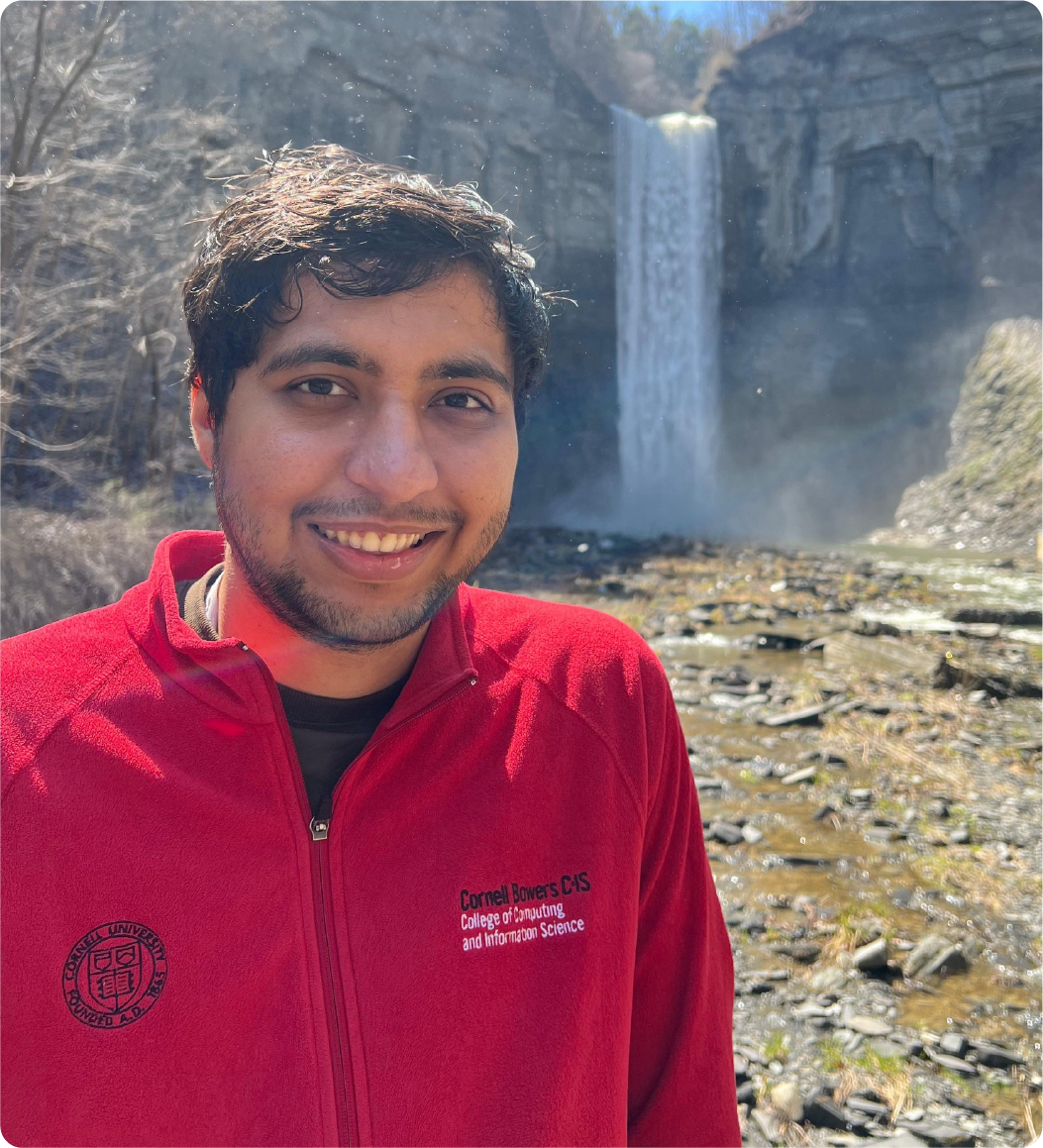 A color photo of a man smiling for a photo with a waterfall in the background.