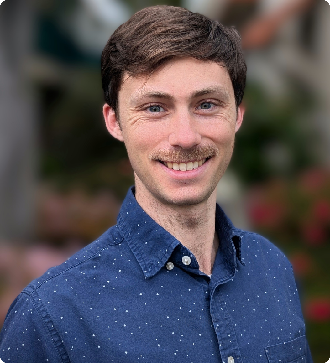 A color photo of a man with a moustache, smiling for a photo.
