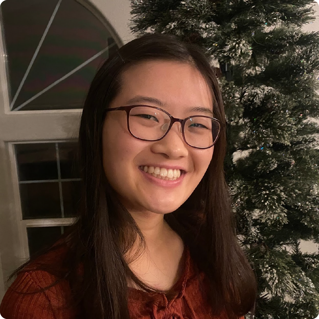 A color photo of a woman smiling for a photo in front of a Christmas tree.