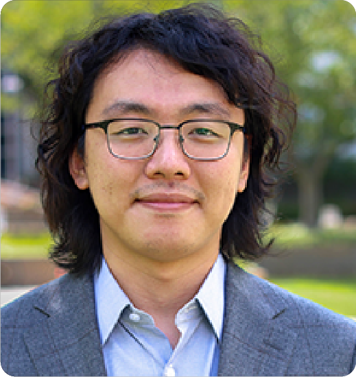 A color photo of a man with glasses, smiling for a photo outside.