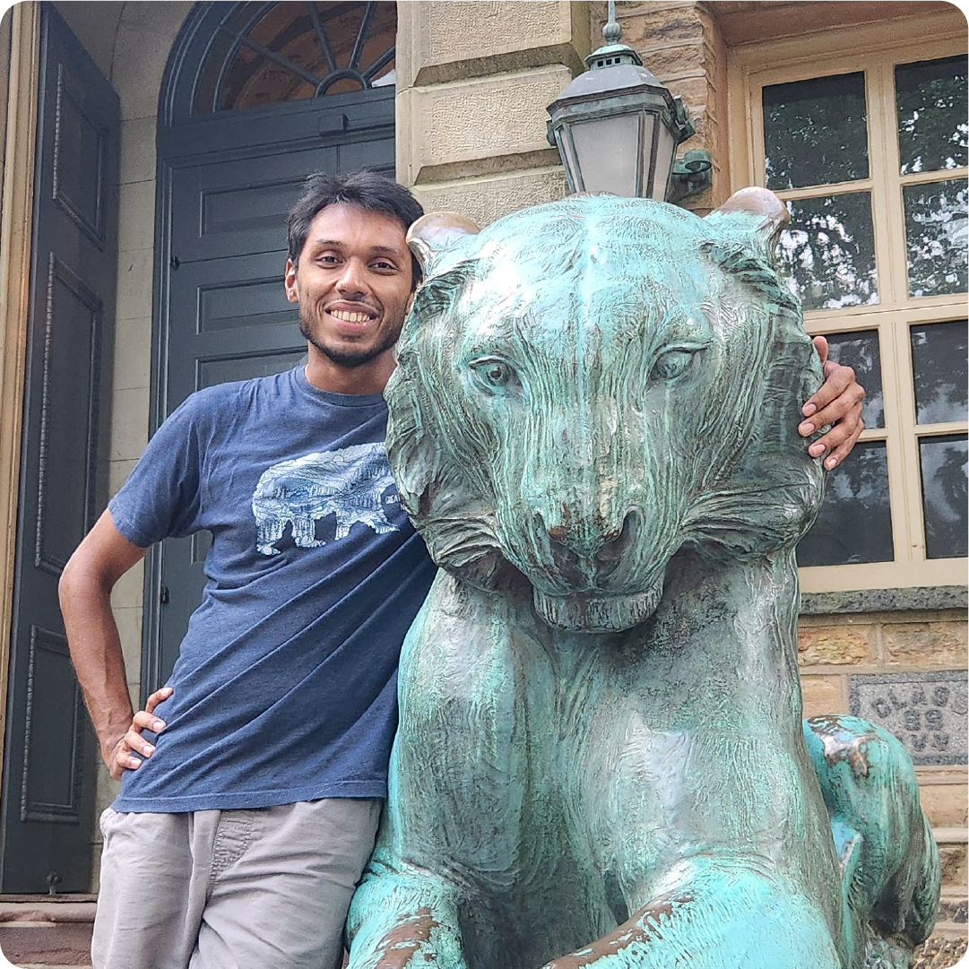 A color photo of a man posing for a photo with his arm around a statue of a large cat.