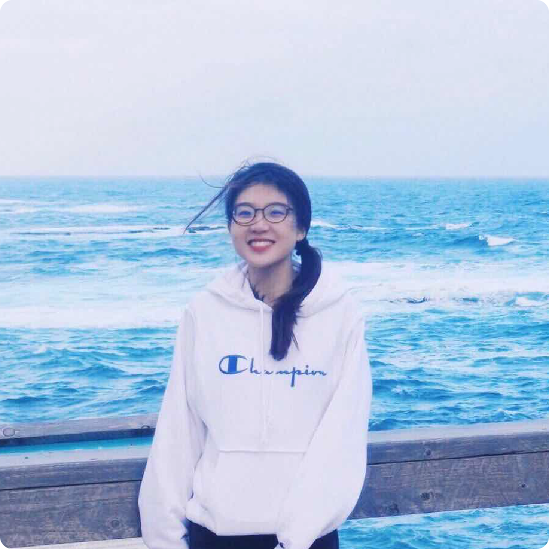 A color photo of a woman standing on a dock, by a large body of water.
