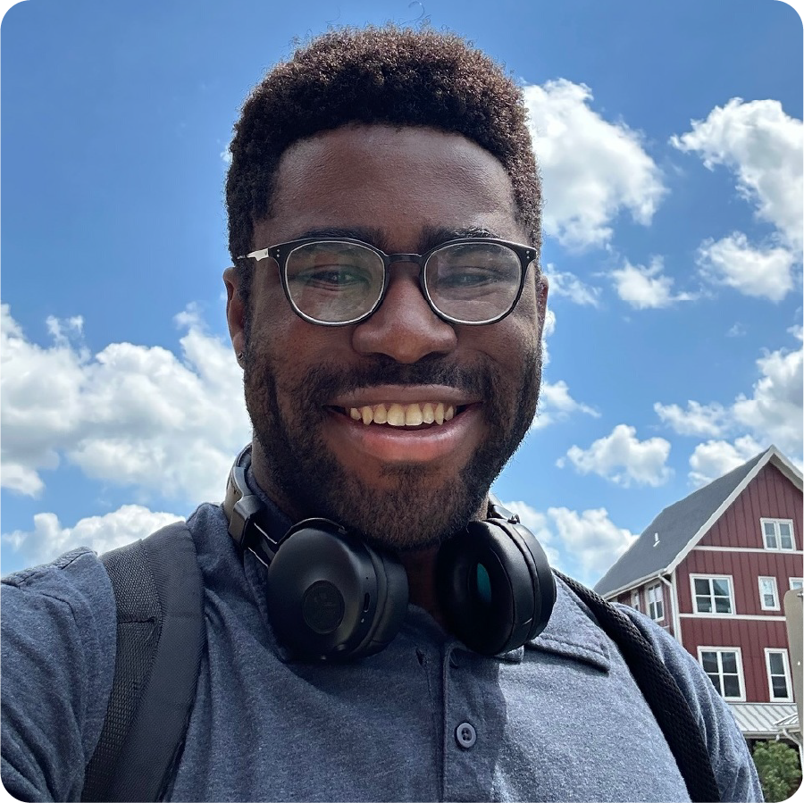 A color photo of a man smiling for a photo outside on a sunny day.