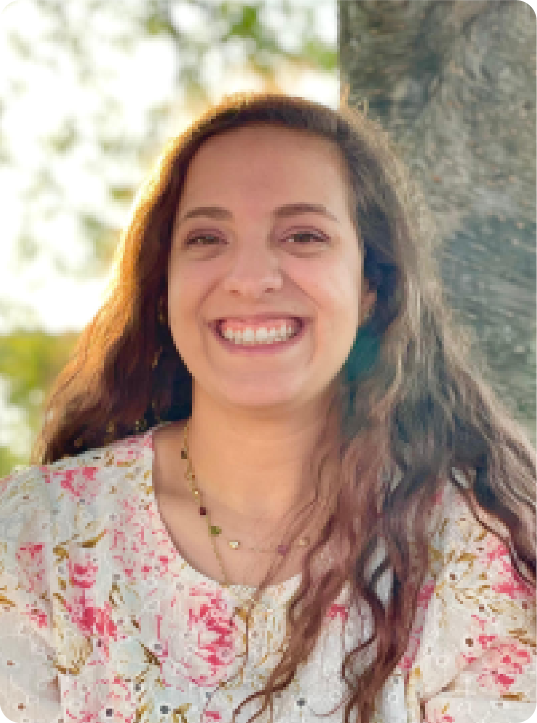 A color photo of a woman smiling for a photo outdoors.