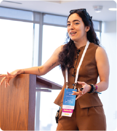 A color photo of a woman speaking next to a podium.