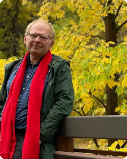 A color photo of a man standing outside in the Fall.