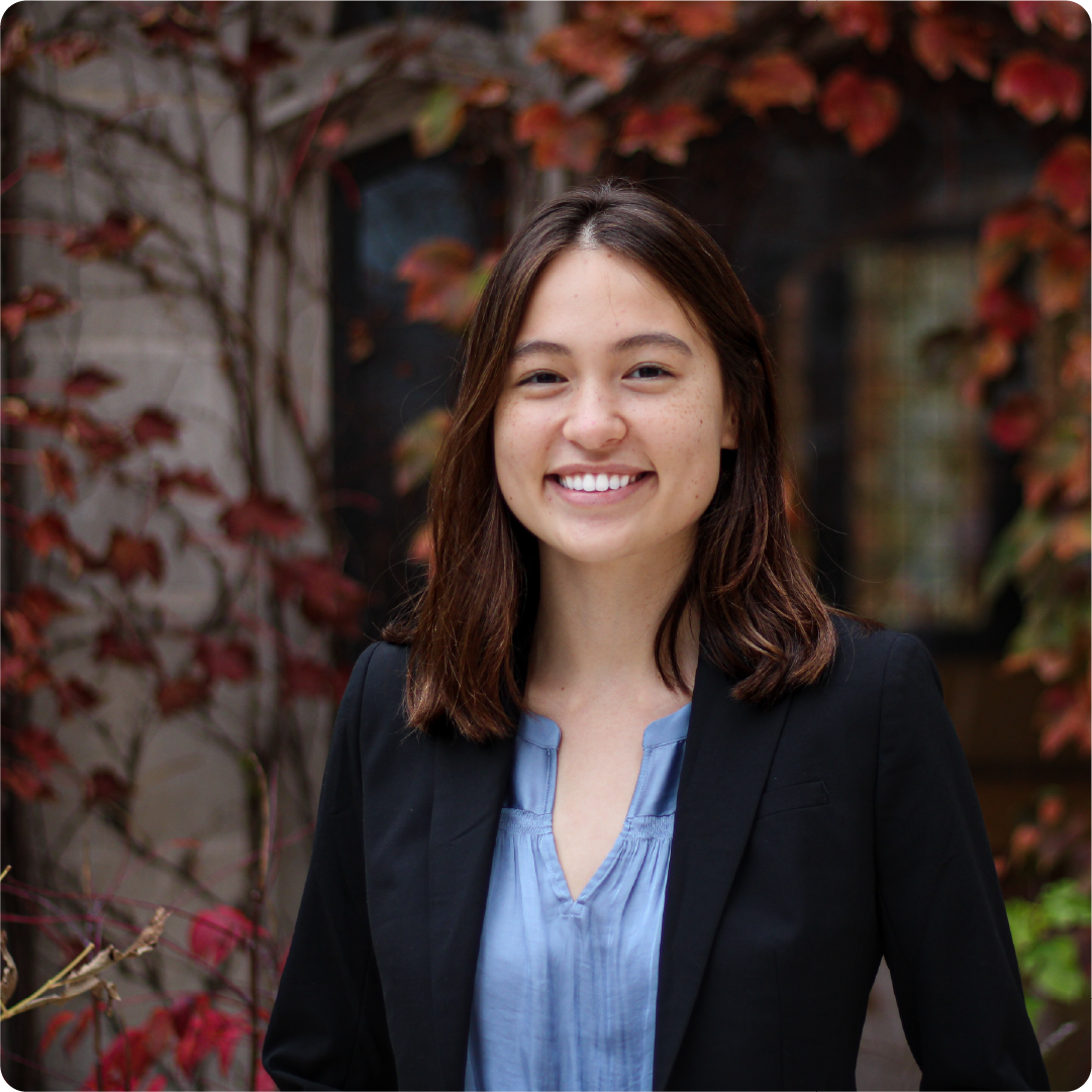 A color photo of a woman standing outdoors, smiling for a photo.