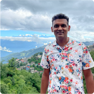 A color photo of a man smiling for a photo on a mountain side.