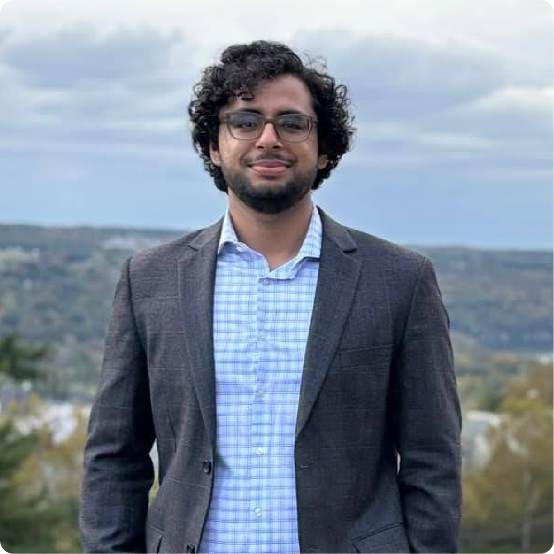 A color photo of a man with a beard smiling for a photo outdoors.