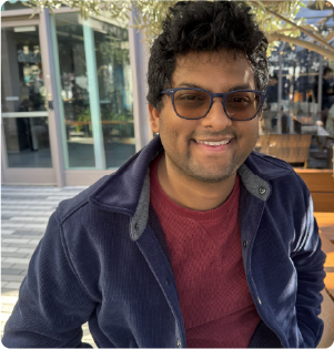 A color photo of a man in sunglasses, smiling for a photo outdoors.