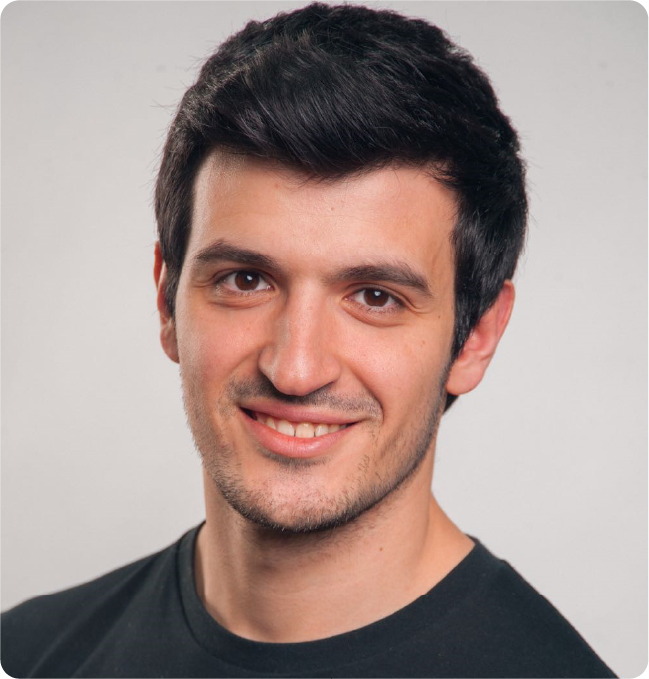 A color photo of a man smiling for a photo wearing a black t shirt.