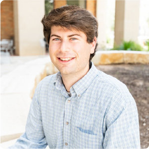A color photo of a man smiling for a portrait outside.