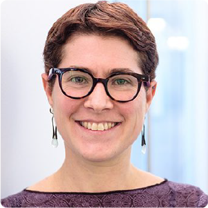 A color photo of a woman with glasses smiling for a photo.
