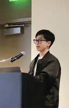 A color photo of a man speaking at a podium