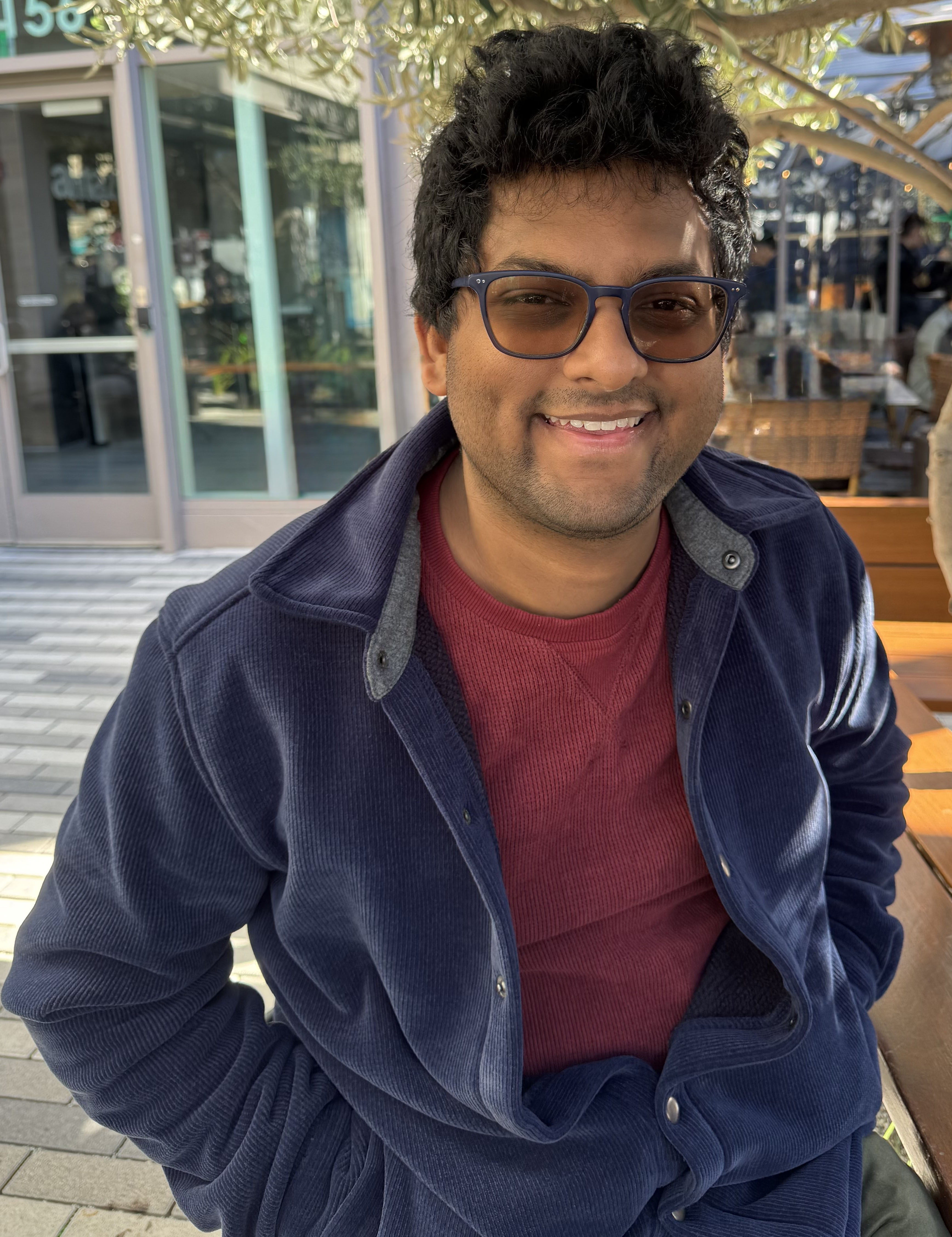 A color photo of a man sitting outdoors, smiling for a photo.