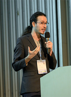 A color photo of a man speaking at a podium.