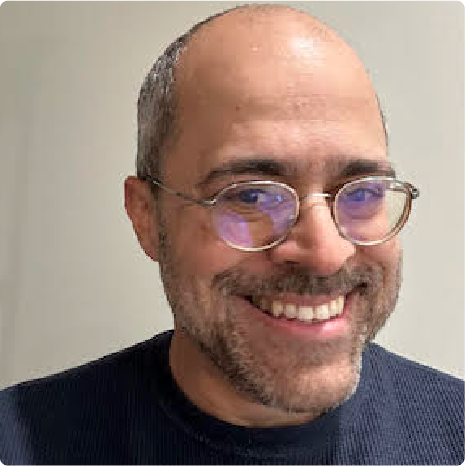 A color photo of a man with glasses smiling for a photo.