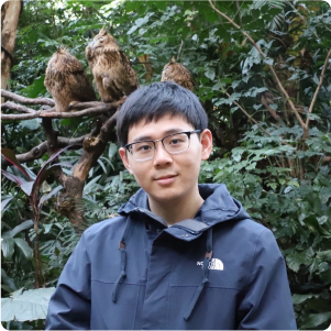 A color photo of a man standing outside at a bird enclosure at a zoo.