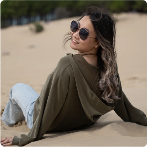 A color photo a woman sitting on the beach looking back over her left shoulder.