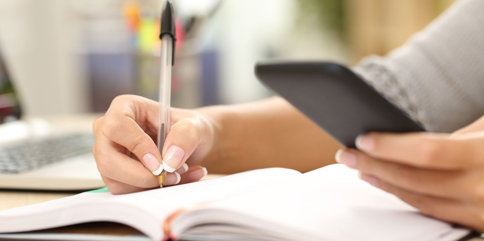 A color photo showing a person using a smart phone and writing down notes. Shutterstock