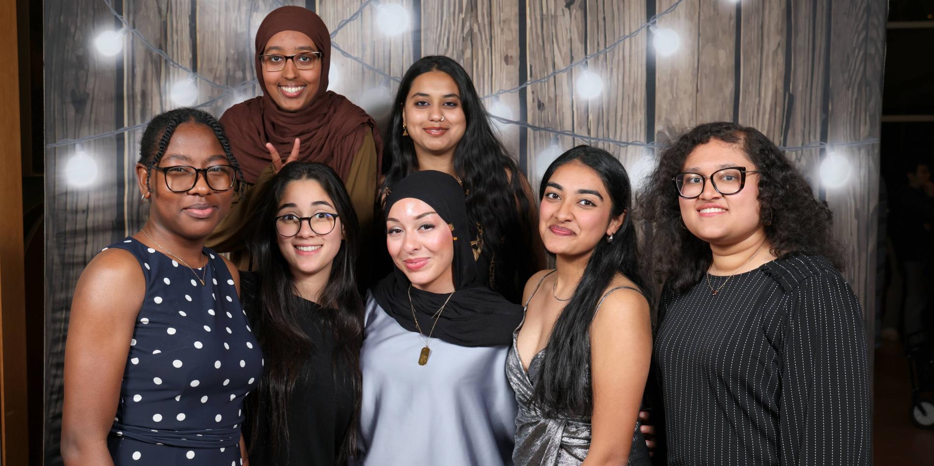 a group of female students poses together against a wooden-like backdrop with lights