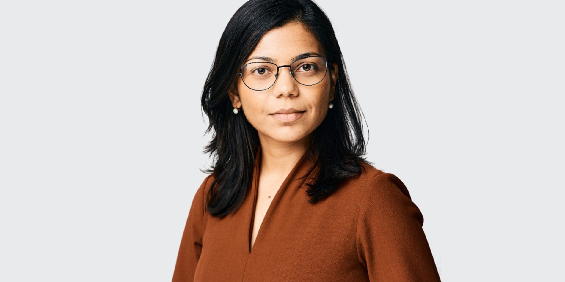 a tan woman with dark hair and glasses wearing a brown shirt 