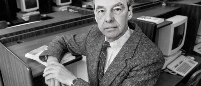 Portrait of Juris Hartmanis in a computer lab with vintage monitors and desks.
