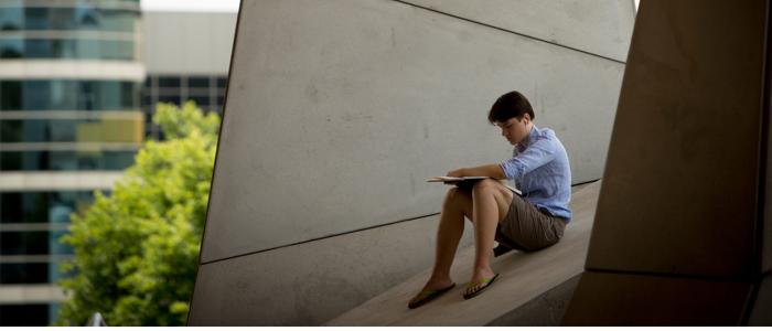 Student sitting on concrete edge working on a notebook