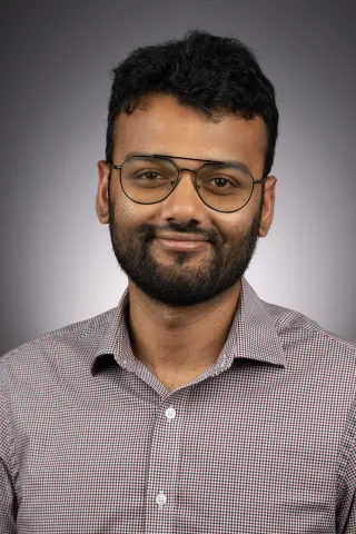 A photo of Eshan Chattopadhyay, a man with dark hair, a beard and glasses in a gray shirt.