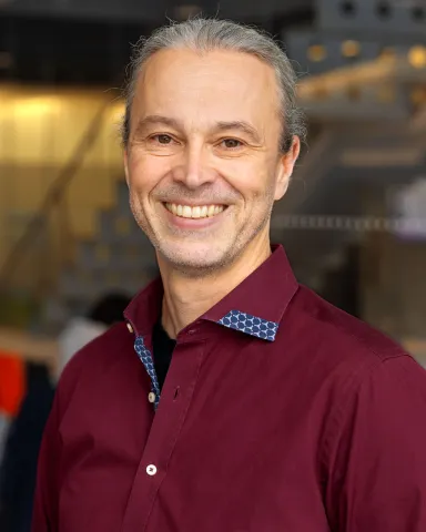 A portrait of Thorsten Joachims, a man with gray hair and a dark red shirt smiling at the camera