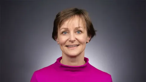 A photo of Anke van Zuylen, a woman with short brown hair in a pink shirt.