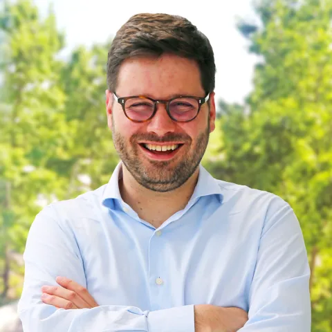 Color portrait of Andrew Owens, smiling at camera. He is wearing a blue shirt and glasses