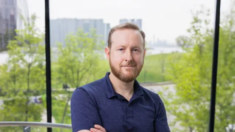 A color photo of a man with a beard standing front of a window for a photo.