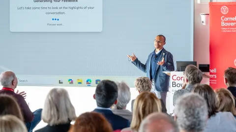 A color photo of a man giving a presentation in front of a large screen.