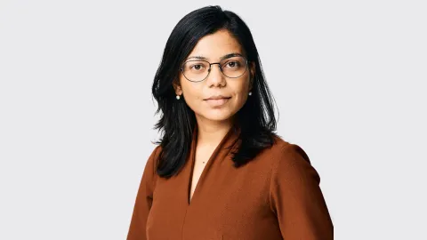 a tan woman with dark hair and glasses wearing a brown shirt 