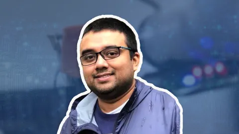 A man with glasses, tan skin and dark short hair smiles in front of a blue overlay background