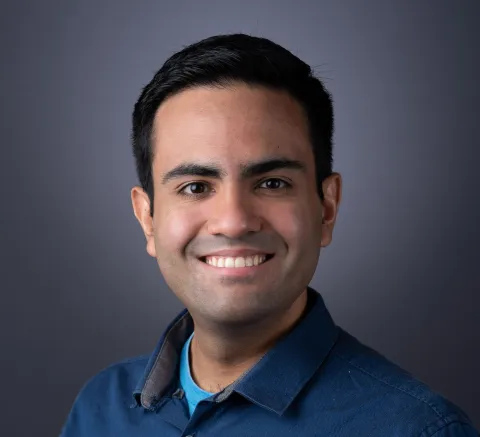 A photo of Christopher De Sa, a smiling man with short dark hair and a blue shirt.