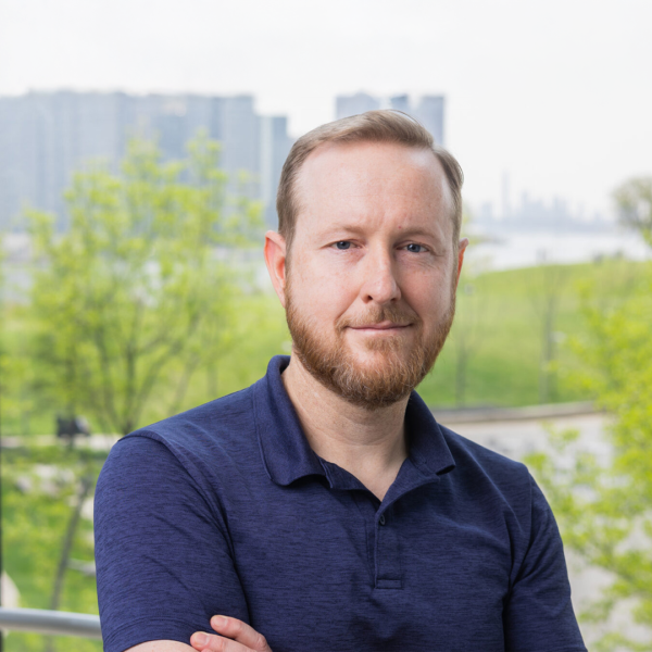 A color photo of a man with a beard standing front of a window for a photo.
