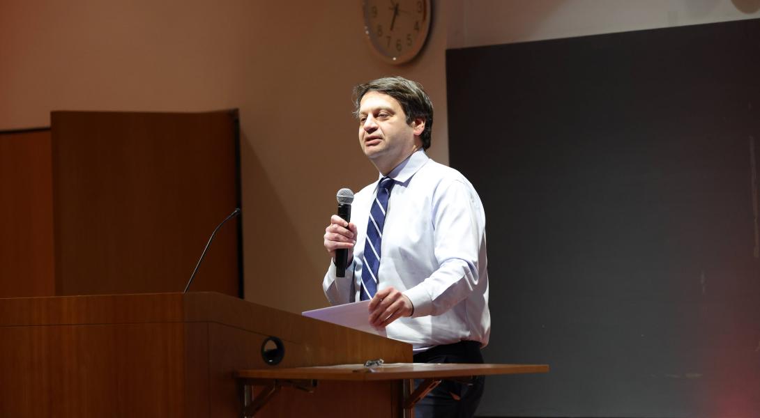 A color photo of a man speaking at a podium.