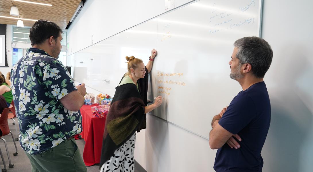 A group of 3 staff members work together, as a female writes on a whiteboard