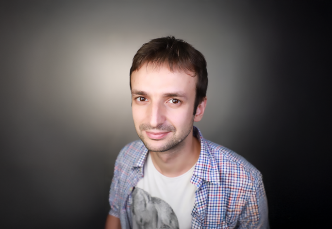 A headshot of a man with short brown hair, wearing a tshirt and button-down