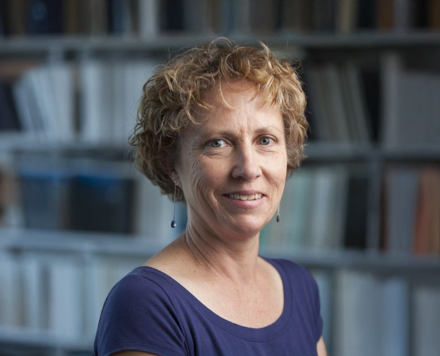 A color photo of woman with short curly hair. Books in background.