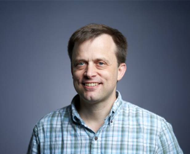 A color photo of Andrew Myers in front of a grey background